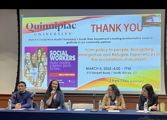 Panelists sit at a table and address an audience.