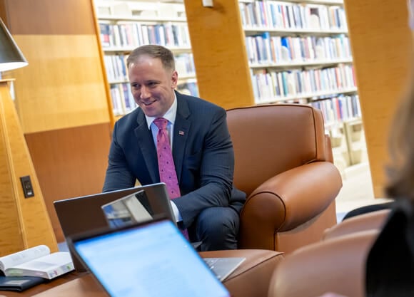 A male professor with an American flag pin working on a laptop in the law library.