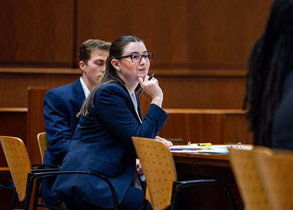 A female student sits at a desk holding a pen in the had she's resting her chin on.