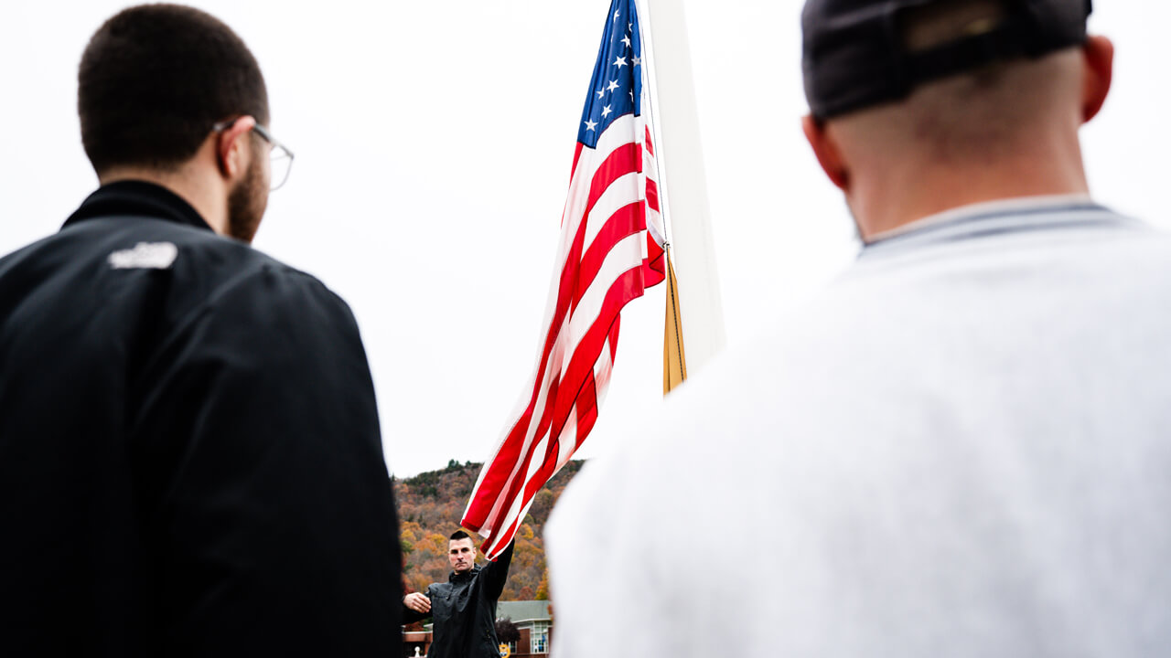 Two veteran students look on as another student raises the American flag on the Quinnipiac quad