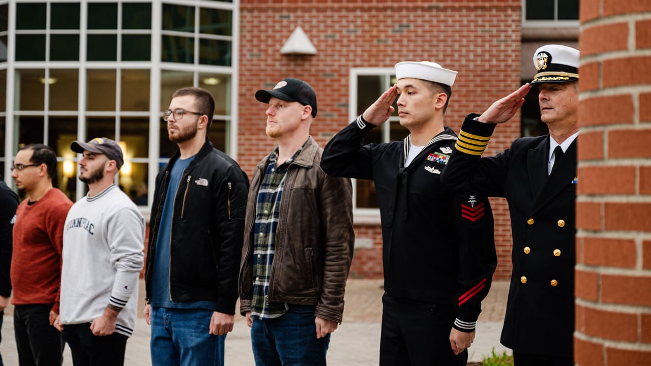 Veteran students in uniform or civilian clothes salute during a flag raising ceremony