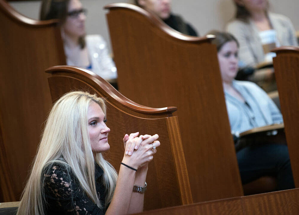 A law student listens to a lecture among a crowd of her classmates in a lecture hall