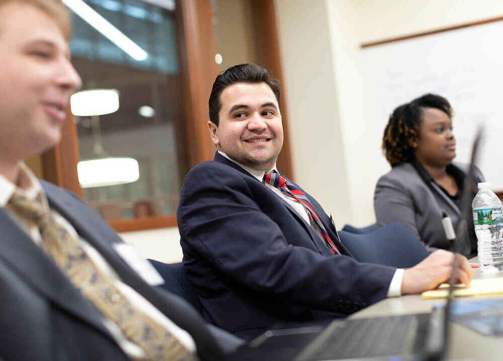 Three law students pictured sitting side-by-side and smiling during a class workshop