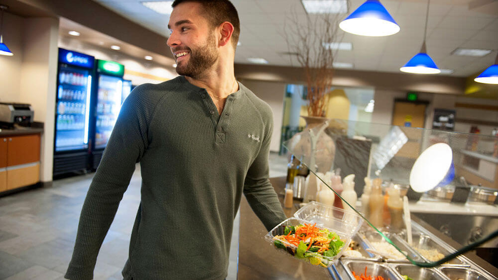A law student holds a salad in the dining area of the North Haven Campus
