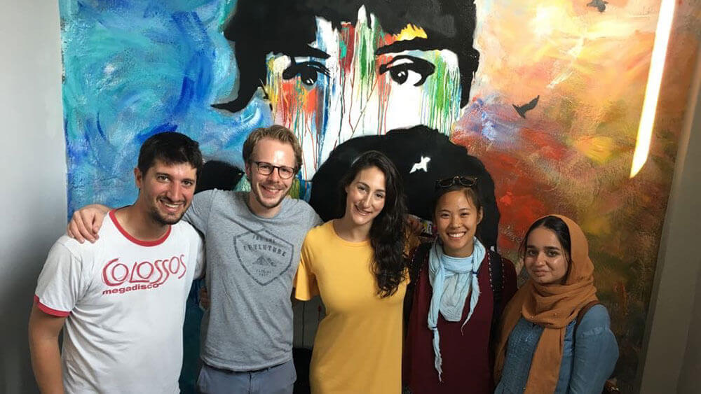 Five law students smile side-by-side in front of a painting in Greece