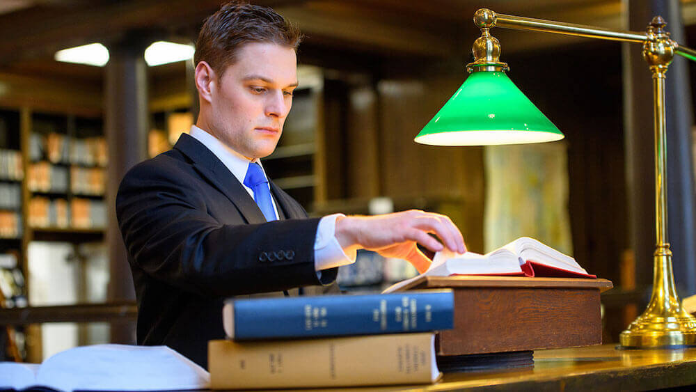 Law alumni Greg Jones reads large textbooks under lamplight in the Connecticut Supreme Court