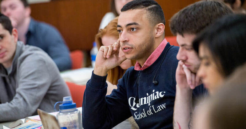 A law student wearing a Quinnipiac Law shirt sits among peers during class