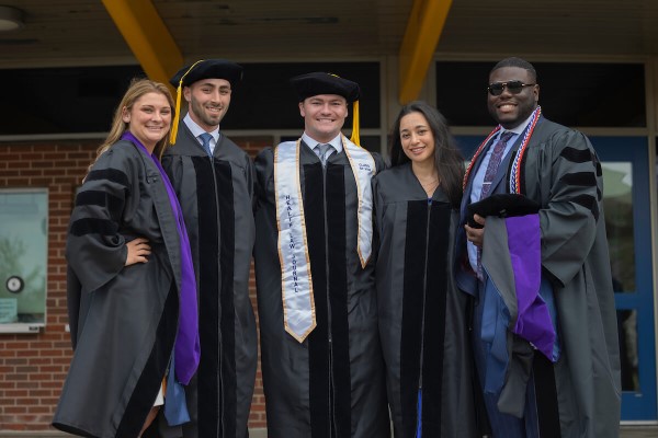 Five law school graduates stand and smile arm in arm for a photo