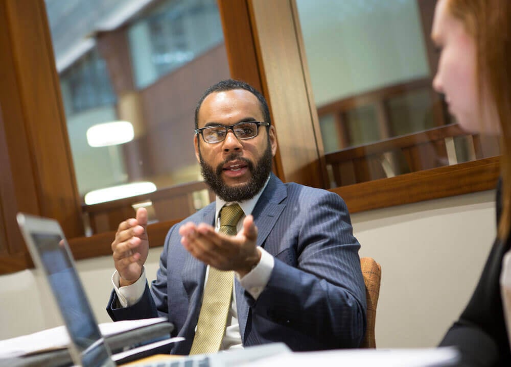 A law student in a suit and tie gestures toward his classmate as he gives his thoughts on a subject