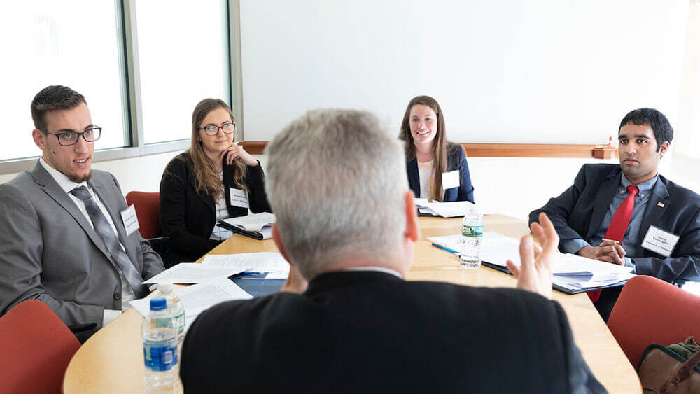 Four law students sit around a table with a professor lecturing at the head